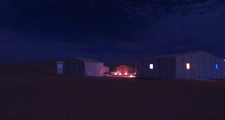 Dimly lit desert tents at night with small lanterns creating a soft glow.