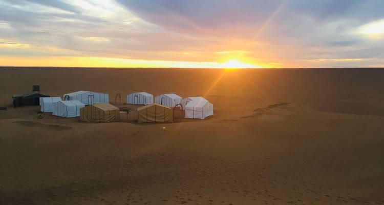 Circle of white desert tents glowing at sunrise on a vast sandy plain.