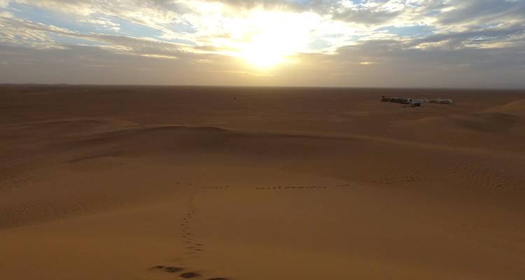 Expansive desert vista at daybreak with long shadows and faint footprints in the sand.