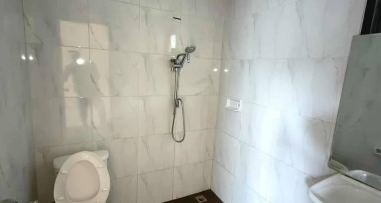 Salle de bains basique carrelée avec toilettes, douche à main et petit lavabo.