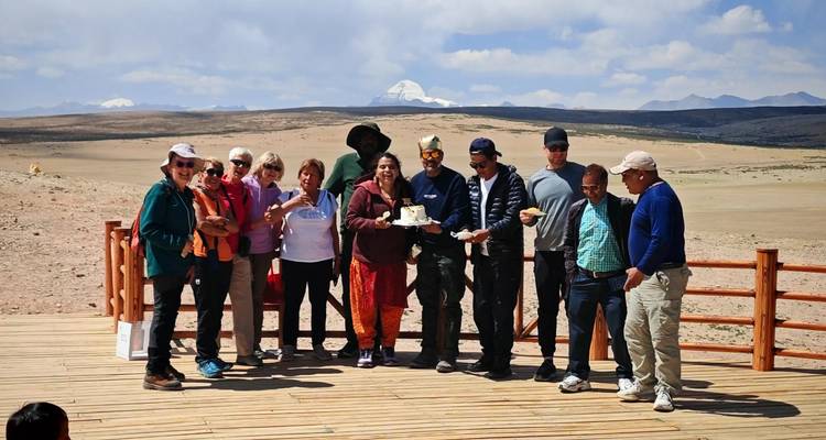 Un plus grand groupe de touristes savoure des rafraichissements sur une terrasse en bois surplombant le vaste plateau avec le Mont Kailash en arrière-plan.