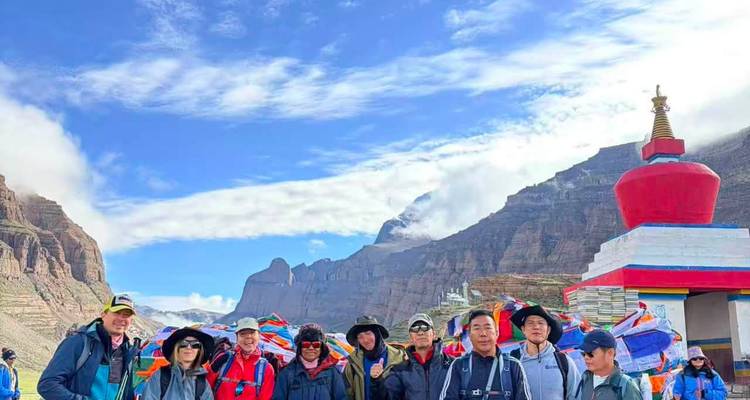 Un groupe de voyageurs se tient à côté d'une stupa colorée et de drapeaux de prière avec des falaises himalayennes spectaculaires en arrière-plan.