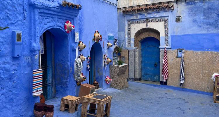 Ruelle d'un bleu éclatant à Chefchaouen avec des chapeaux faits à la main et des tabourets exposés devant les portes.