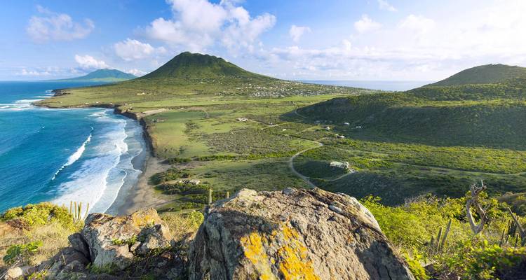 Amplio panorama costero de paisaje verde ondulante, picos volcánicos y olas que se estrellan