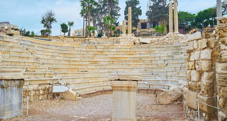 Ruinen eines römischen Amphitheaters mit gestuften Marmorsitzen, umgeben von Grünflächen in Alexandria.