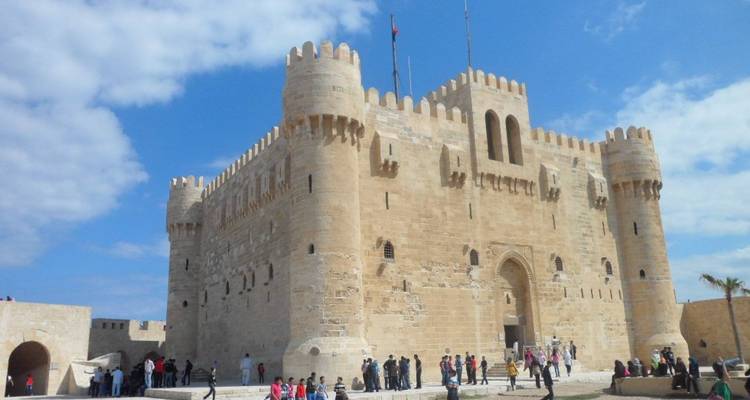 Menschenmengen außerhalb der sandfarbenen Zitadelle von Qaitbay unter einem teilweise bewölkten Himmel.