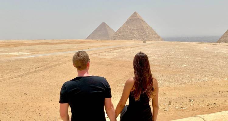 Couple holding hands while gazing toward the three pyramids on the Giza plateau.