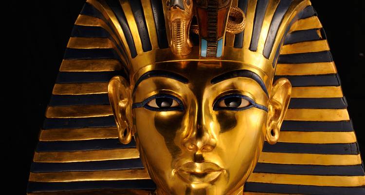 Close-up of the golden funerary mask of Tutankhamun displayed against a dark background.