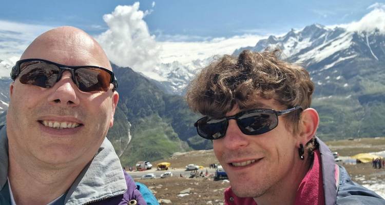 Two travellers in sunglasses take a selfie with snowy Himalayan peaks in the background