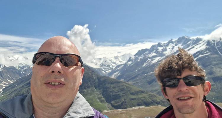 Selfie of two travellers with rugged snow-clad mountains and blue sky behind them