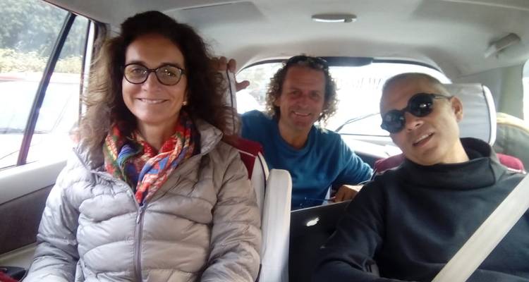Three travellers sitting in the back seat of a car smiling at the camera during a road trip