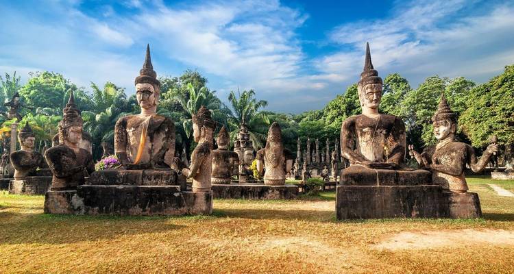 Row of large stone Buddha statues surrounded by palm trees under a bright blue sky in Buddha Park.