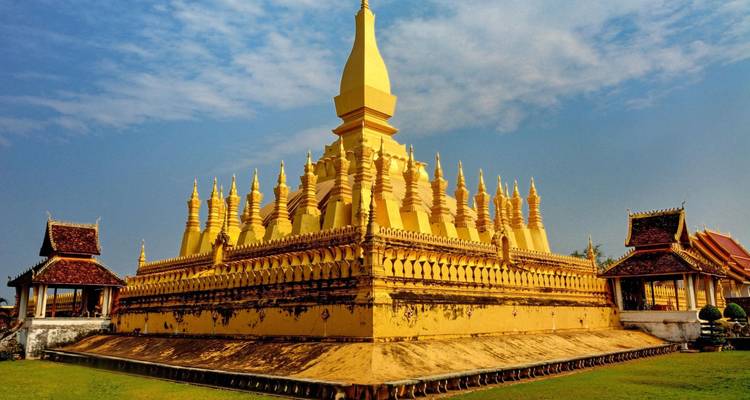 Side perspective of the gilded Pha That Luang complex with ornate tiers under soft morning light.