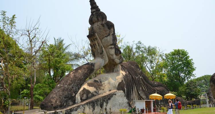 Giant reclining Buddha statue resting on its elbow in a grassy park with visitors nearby.