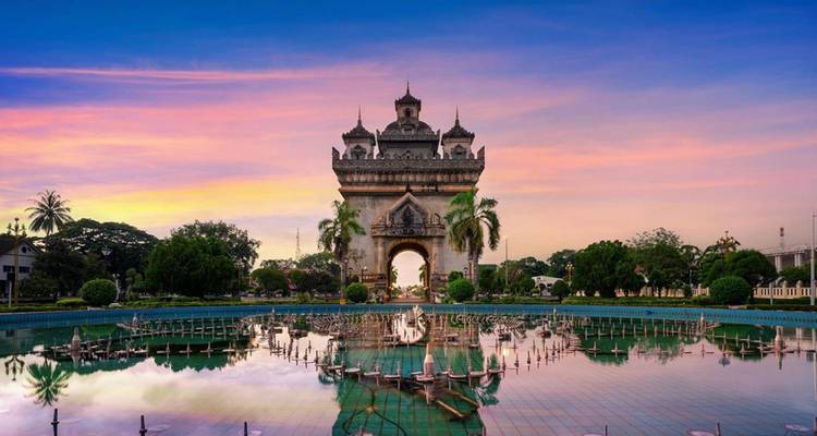Patuxai Victory Gate reflected in a still pool under vivid sunrise colours in Vientiane