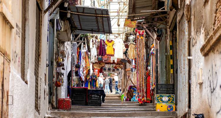 Colourful narrow souk alley with hanging garments, rugs and shoppers in the distance