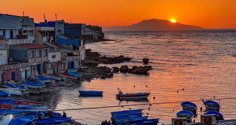 Fishing village with blue boats at golden sunset over calm Mediterranean waters