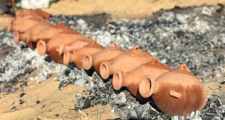 Row of traditional clay pots firing over grey embers in desert setting
