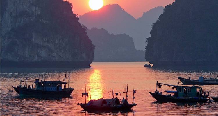 Fishing boats silhouetted on calm water at sunset among limestone karsts of Halong Bay