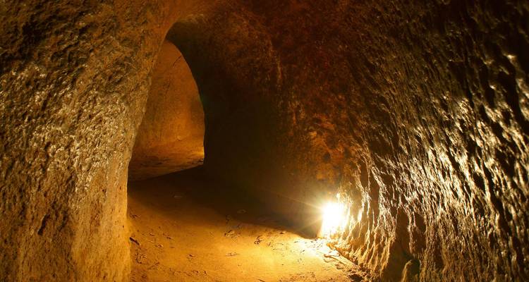 Dimly lit earthen tunnel passage with a warm spotlight illuminating the rough walls