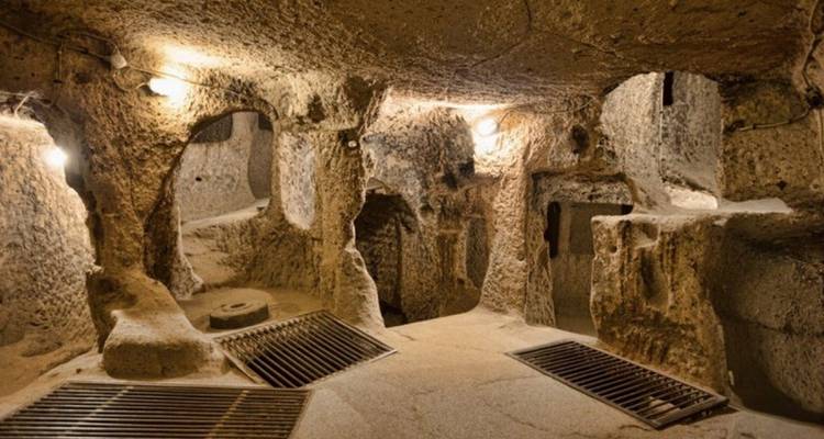 Underground chamber with stone carved rooms and metal grates on the floor lit by small bulbs
