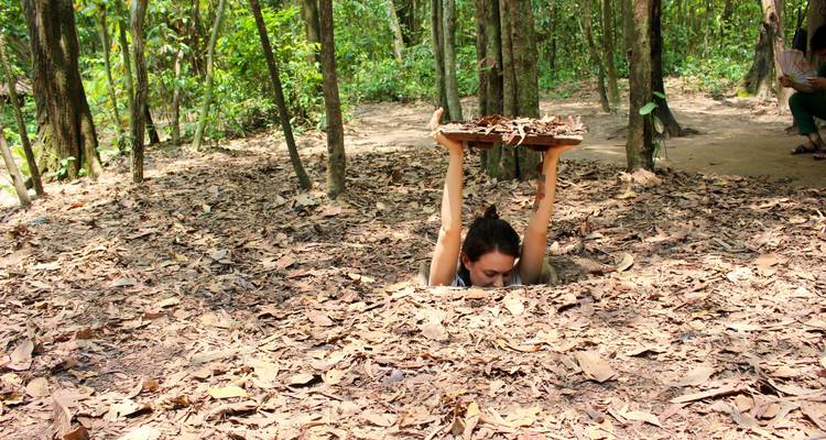 Young woman emerging from a narrow tunnel entrance in a forest floor while lifting a wooden cover