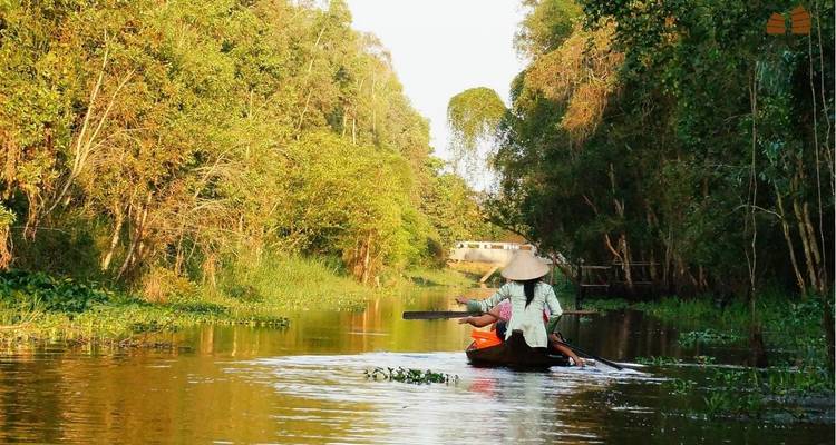 Small wooden sampan with two people paddling through a narrow tree-lined waterway