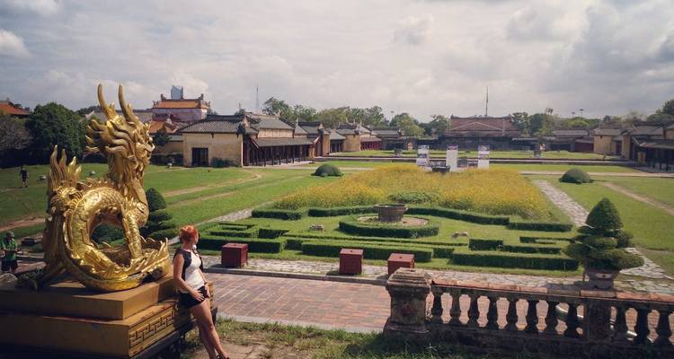 Traveller rests by a golden dragon sculpture overlooking manicured gardens of an imperial citadel