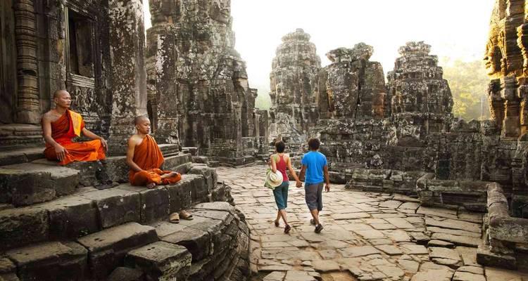 Two monks and two tourists explore ancient stone ruins with dramatic columns and carvings