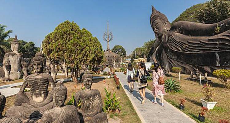 Des visiteurs se promenant parmi des sculptures de Bouddha en pierre fantaisistes dans un parc extérieur ensoleillé