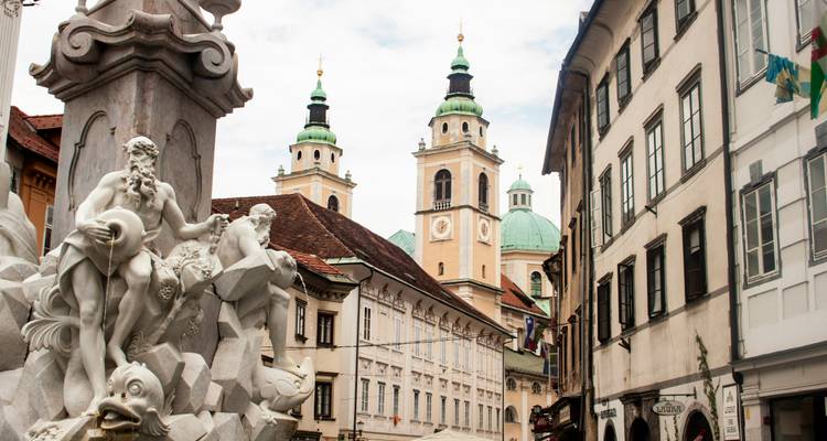 Barokke Robba-fontein in Ljubljanas oude stad met de tweeling groene koepels van de Sint-Nicolaaskerk daarboven.