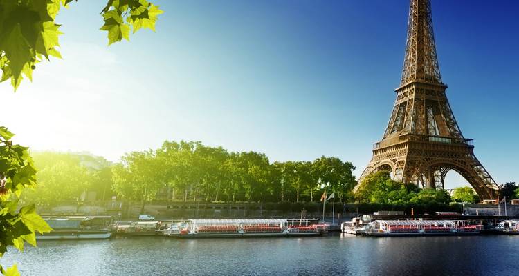 El sol de la madrugada ilumina la Torre Eiffel junto al Sena tranquilo con barcos fluviales amarrados.