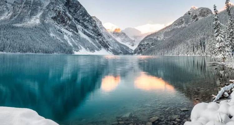 Kristallklares Wasser des Lake Louise, das schneebedeckte Gipfel während eines ruhigen Wintersonnenaufgangs widerspiegelt.