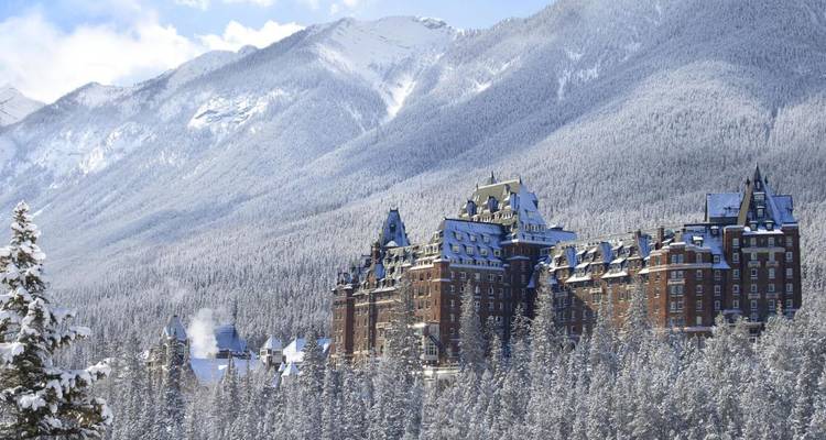 Das historische Fairmont Banff Springs Hotel liegt eingebettet in einen dichten, verschneiten Wald am Fuße dramatischer Berge.