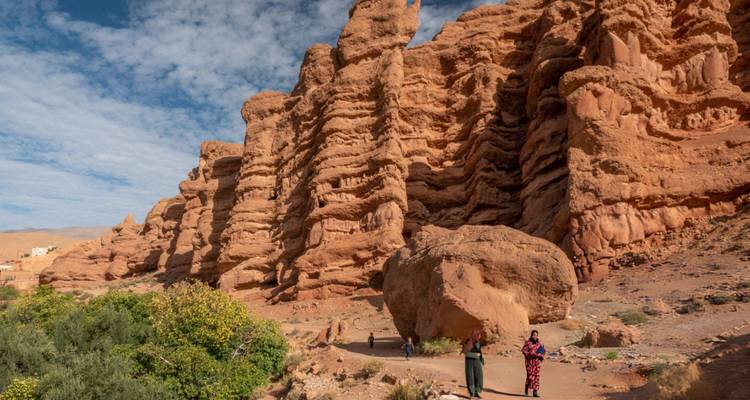 Red sandstone cliffs and rock formations tower above walkers on a desert trail