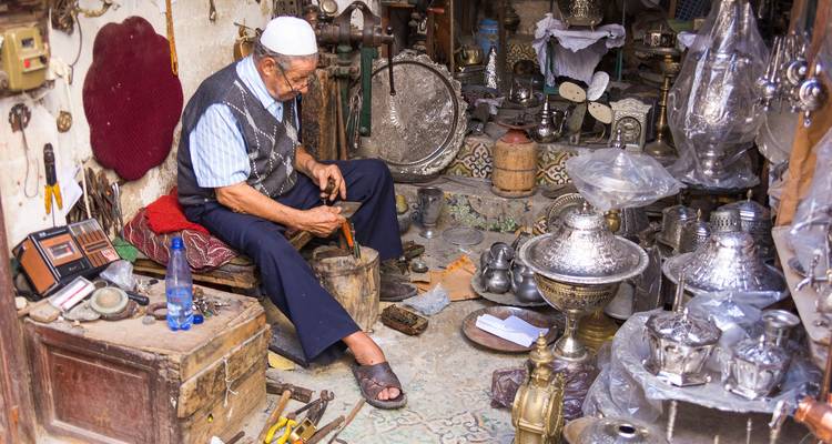 Artisan hammering metalware in a traditional Moroccan workshop cluttered with tools