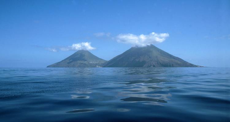 Twin volcanic cones emerging from a tranquil sea with light clouds at their summits