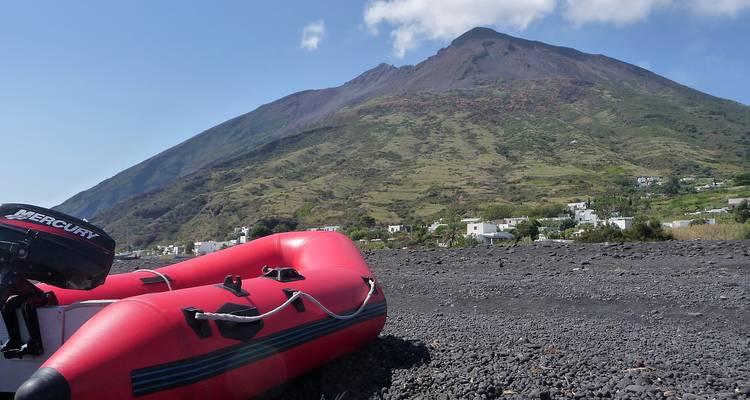 Red inflatable dinghy resting on black volcanic beach with Stromboli volcano in background
