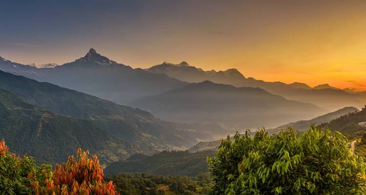 Vue panoramique du lever de soleil sur les montagnes himalayennes en étages avec le pic distinctif de Machapuchare et les vallées verdoyantes luxuriantes au premier plan.