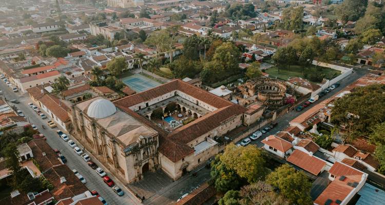 Vista aérea con dron de las manzanas coloniales de la ciudad de Antigua y ruinas de convento rodeadas de tejados de barro cocido.