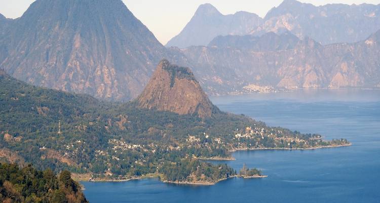 Vista panorámica del Lago Atitlán y los volcanes que lo rodean bajo la luz de la tarde brumosa.