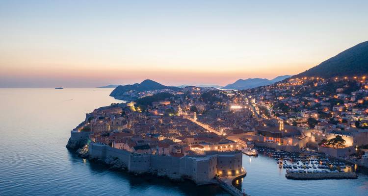 Aerial twilight view of Dubrovnik’s walled old town illuminated beside the Adriatic Sea.