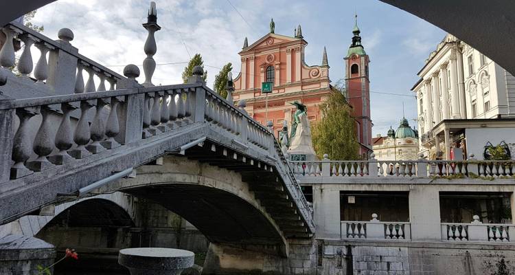 Stone Triple Bridge and pink Franciscan Church viewed from beneath an arch in Ljubljana’s old town.