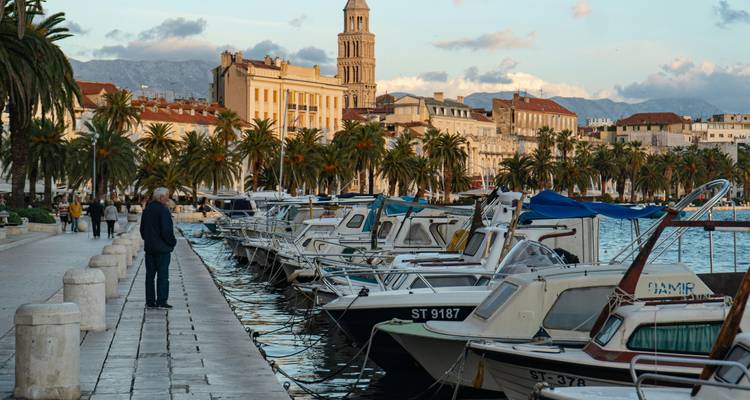 Boats lined along Split’s palm-fringed Riva promenade with Diocletian’s Palace bell tower at golden hour.
