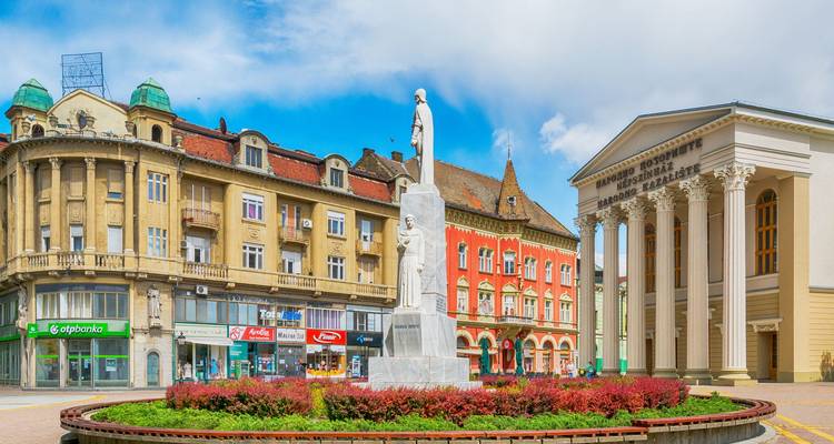 Farbenfroher historischer Platz mit zentraler Marmorstatue und prunkvollen Gebäuden unter einem strahlend blauen Himmel in Novi Sad.