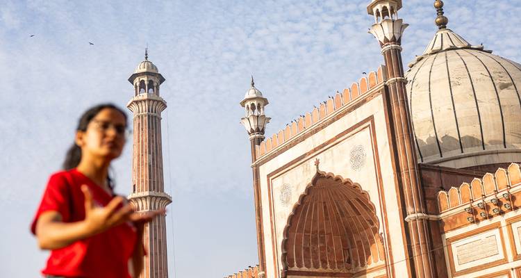 Viajero desenfocado gesticulando frente a la gran mezquita Jama Masjid con sus altos minaretes.