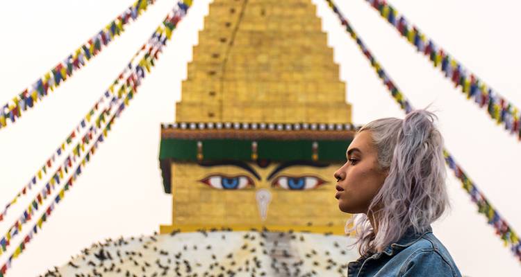Perfil lateral de una joven frente a la dorada Estupa de Boudhanath adornada con banderas de oración.