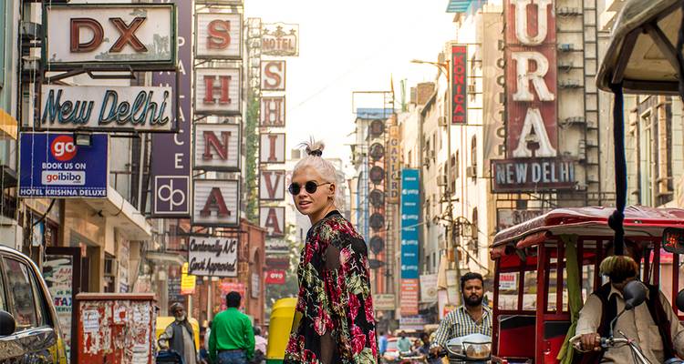 Un viajero de moda camina por una concurrida calle de Nueva Delhi llena de letreros de neón.