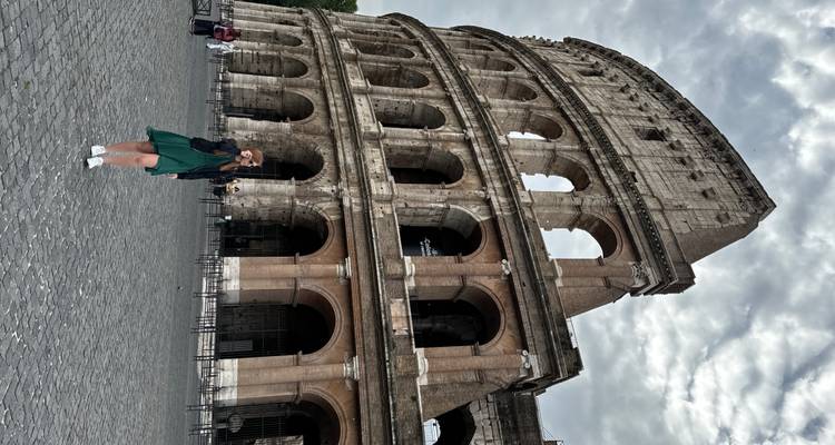 Vrouw in groene jurk die de massieve gevel van het Colosseum fotografeert op een bewolkte ochtend.