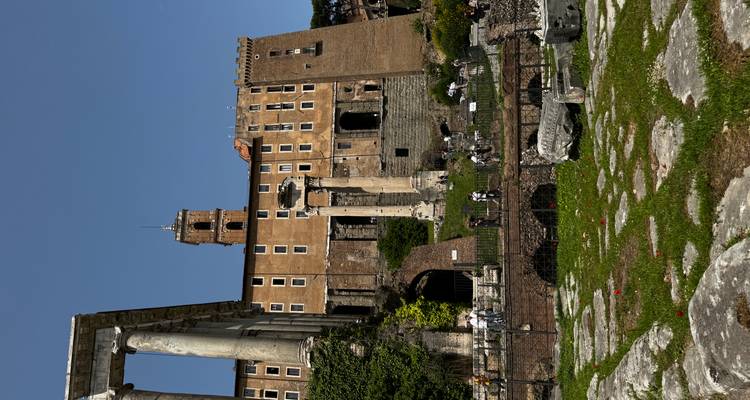 Ruïnes van het Romeinse Forum met staande zuilen en een middeleeuwse toren tegen een stralend blauwe lucht.